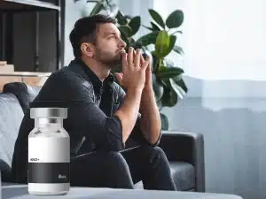 Person holding head in stress next to NAD supplement bottle, representing possible anxiety side effects of NAD therapy.